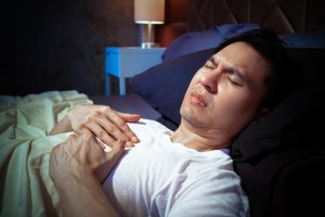man holding his chest having a hard time sleeping