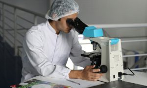 man in white coat examining samples in microscope